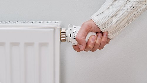 Foto einer Hand, die an einem Heizungsthermostat dreht