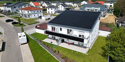 Foto, Mehrfamilienhaus aus der Vogelperspektive mit Photovoltaikmodulen auf dem Dach.