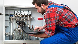 Foto, ein Techniker mit Laptop kniet vor einer Heizungsanlage