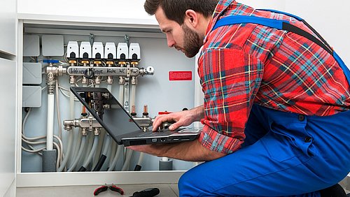 Foto, ein Techniker mit Laptop kniet vor einer Heizungsanlage