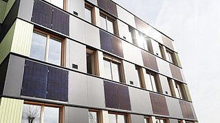 Foto, Mehrstöckiges Gebäude mit Fassadenverkleidung aus Solarpaneelen und Fenstern unter bewölktem Himmel