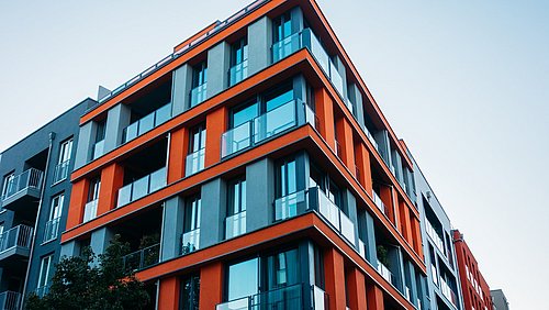 Foto, Blick hinauf an der Fassade eines mehrstöckigen Neubaus mit auffälligen roten Fassadenelementen.