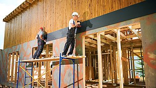 Foto, zwei Handwerker arbeiten an der Fassade eines Neubaus aus Holz.